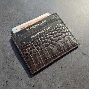 Front view of a dark brown leather card case featuring a luxury croc-embossed texture and three card slots filled with cards and cash.